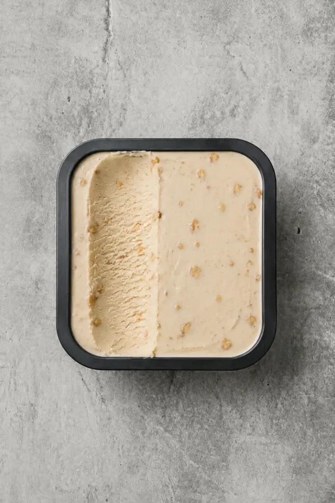 Bola de helado de turrón artesanal, de color beis, en una tarrina